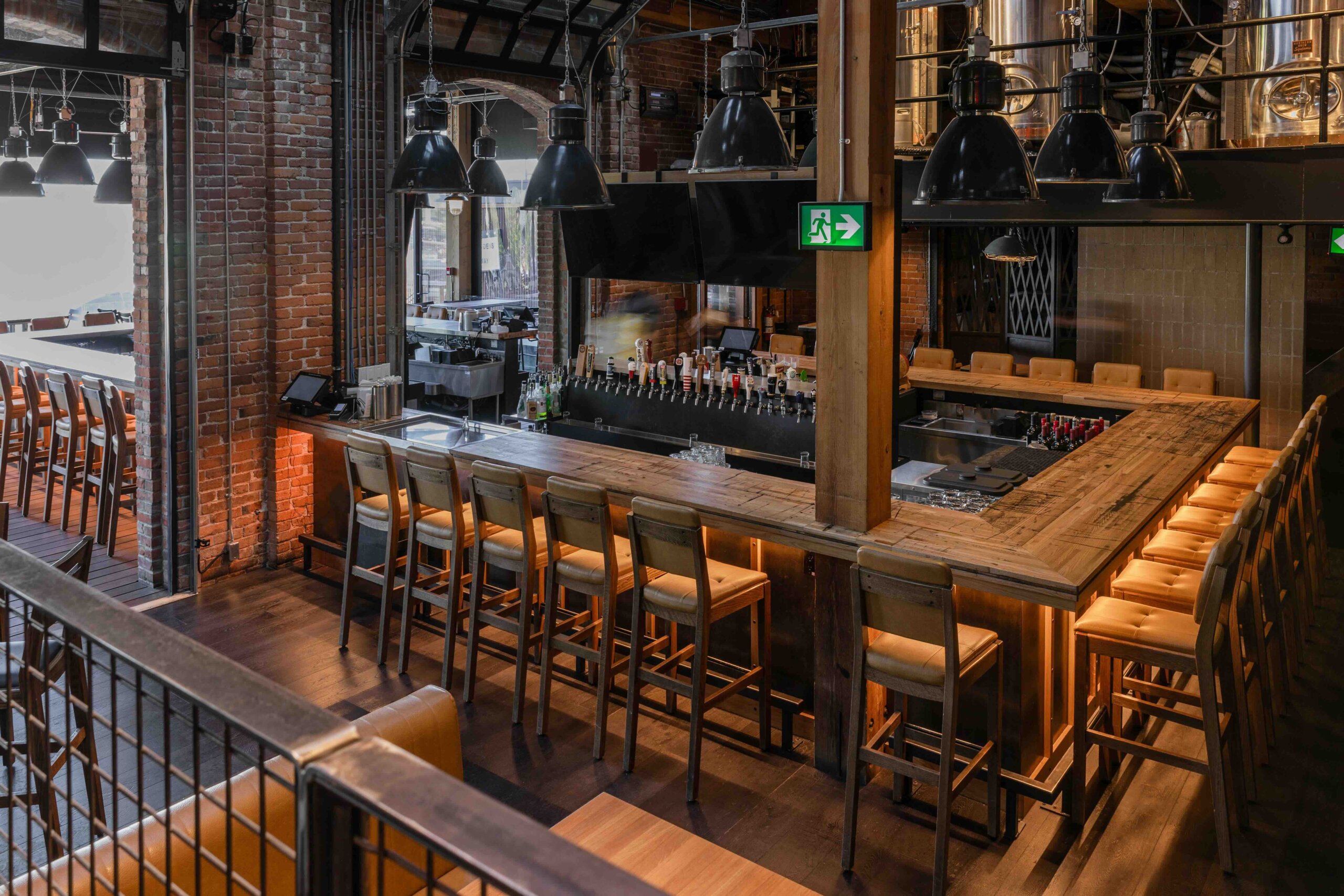 CRAFT Beer Market A modern bar with wooden counters, high chairs, multiple beer taps, industrial lighting, and brick walls in a spacious, empty setting.