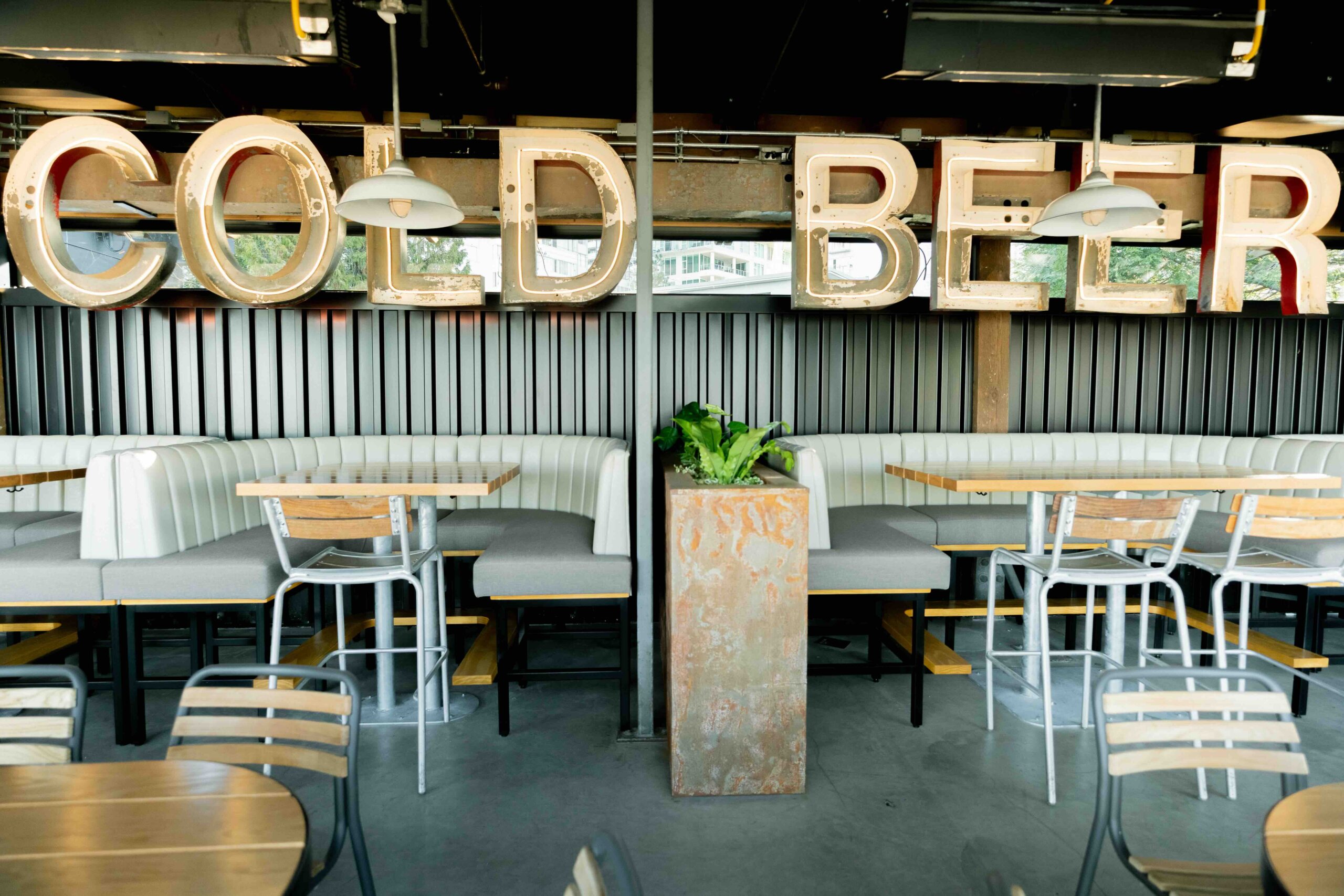 CRAFT Beer Market A modern bar seating area with metal chairs, cushioned booths, and a large illuminated "COLD BEER" sign on the wall.