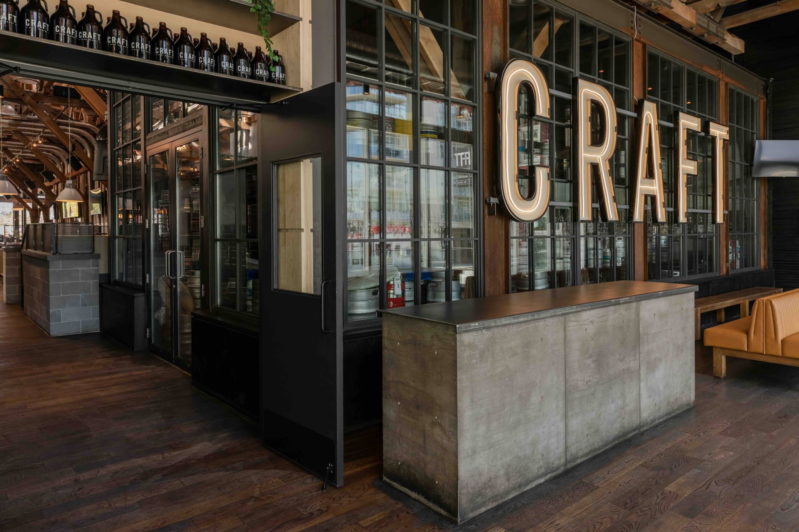 CRAFT Beer Market Interior of a modern restaurant with wooden floors, metal counter, large windows, bottles on display, and a prominent “CRAFT” sign on the wall—perfect for casual dining and enjoying inventive craft cocktails.