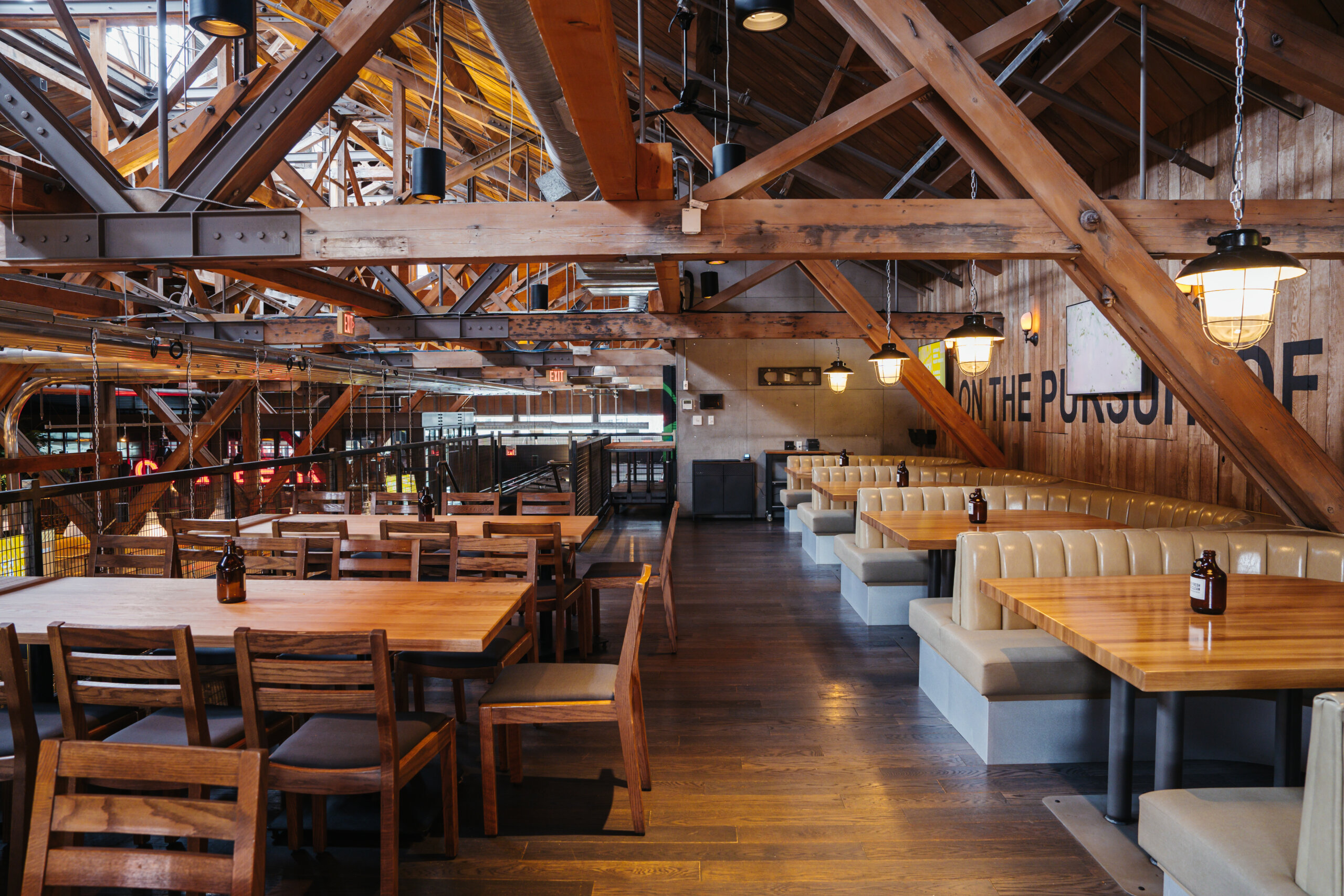 CRAFT Beer Market A spacious restaurant interior with exposed wooden beams, wooden tables and chairs, beige booth seating, and hanging lights—perfect for enjoying craft beer and soaking up the social vibes.