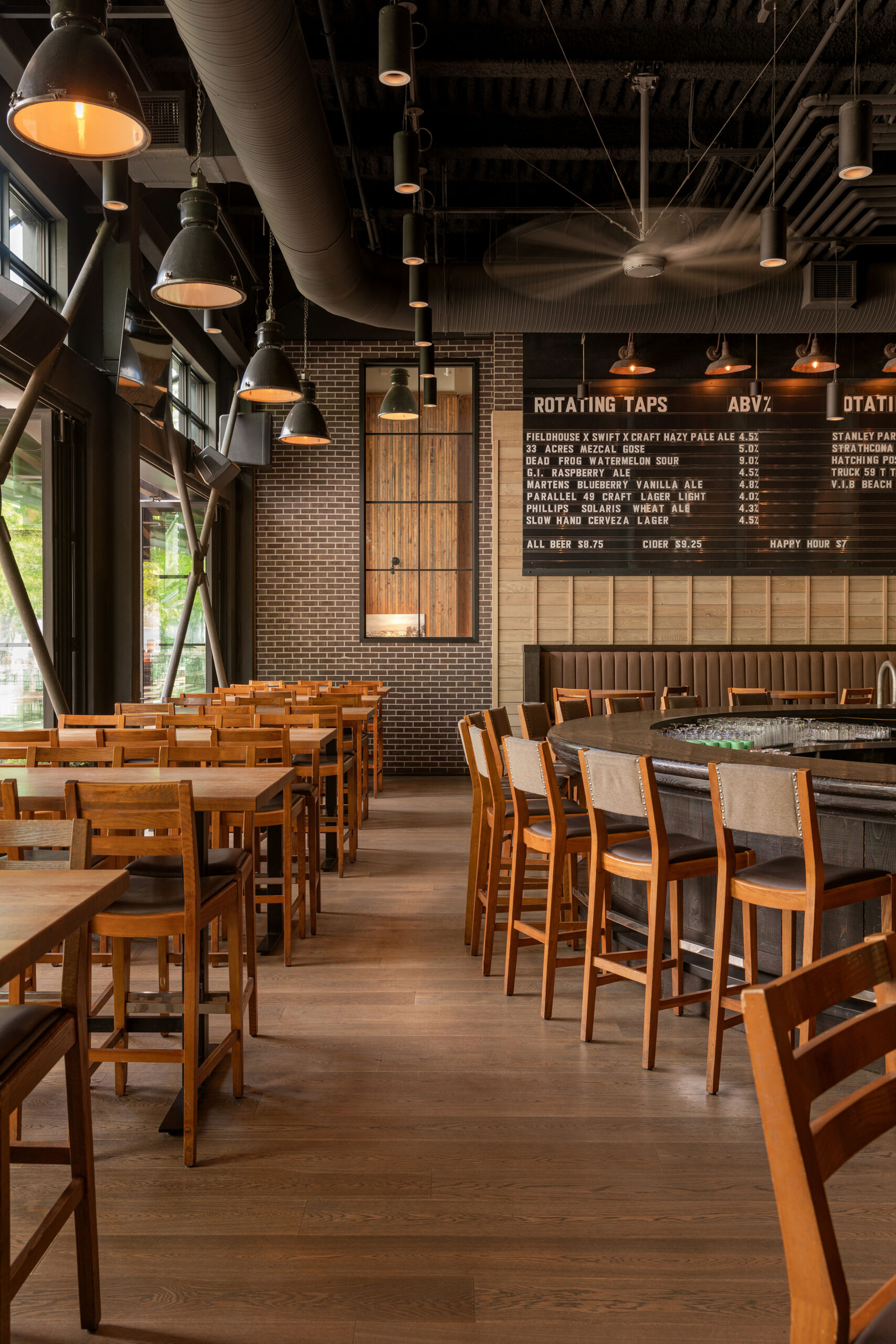 CRAFT Beer Market Modern bar interior with wooden tables and chairs, a long counter with barstools, industrial ceiling, and a large menu board listing rotating craft beers. Perfect for group bookings or casual nights out.