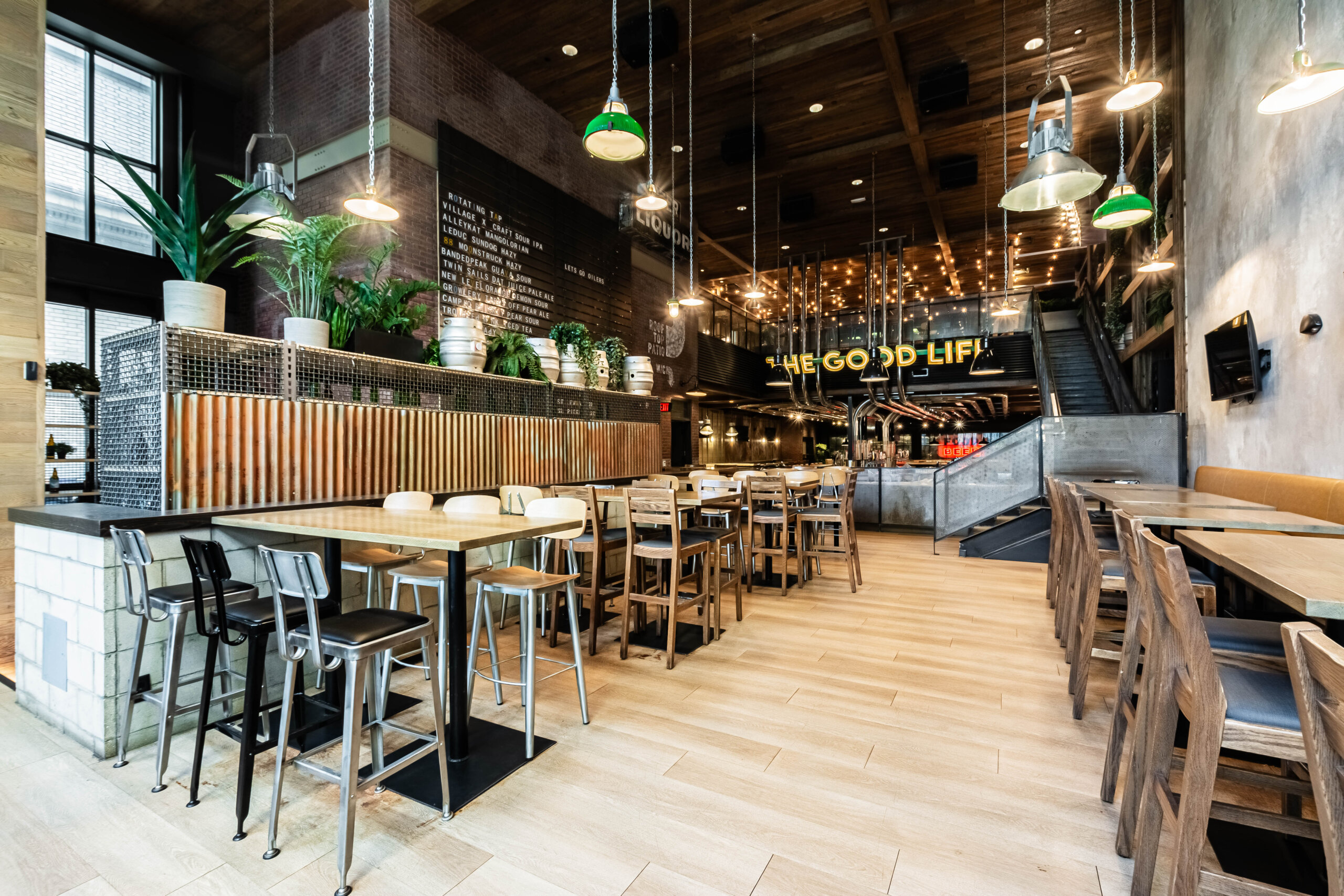 CRAFT Beer Market Modern restaurant interior with wooden tables and chairs, industrial lighting, plants, and "THE GOOD LIFE" sign in the background. The space features sustainable design elements and a clean, well-lit atmosphere.