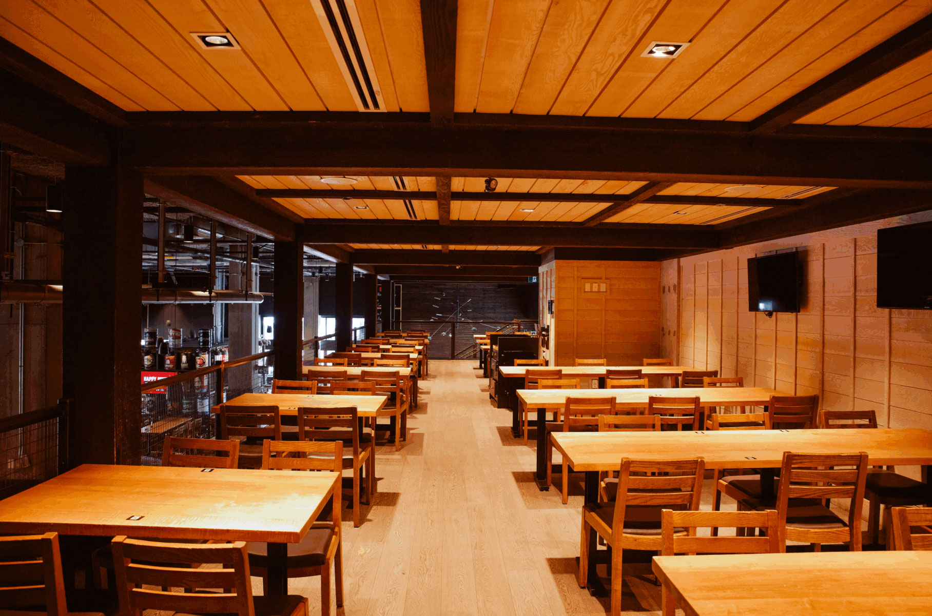 CRAFT Beer Market Spacious restaurant interior with wooden tables and chairs arranged in rows, warm lighting, flat-screen TVs on the walls, and a lively atmosphere perfect for enjoying craft cocktails and social vibes.