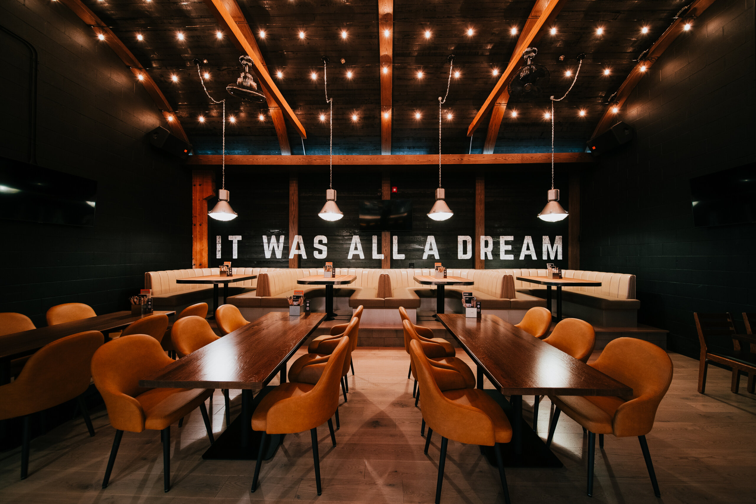CRAFT Beer Market Modern restaurant interior with warm lighting, orange chairs, wooden tables, and a sign on the back wall that reads "IT WAS ALL A DREAM," offering craft beer and rotational taps for a unique dining experience.