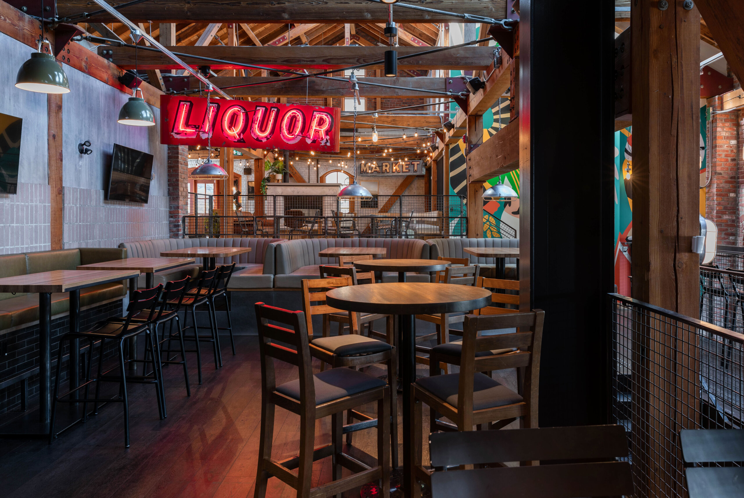 CRAFT Beer Market Industrial-style bar interior with wooden beams, tables, and chairs, booths along the wall, and a large red neon "LIQUOR" sign hanging from the ceiling—perfect for social vibes and enjoying creative craft cocktails.