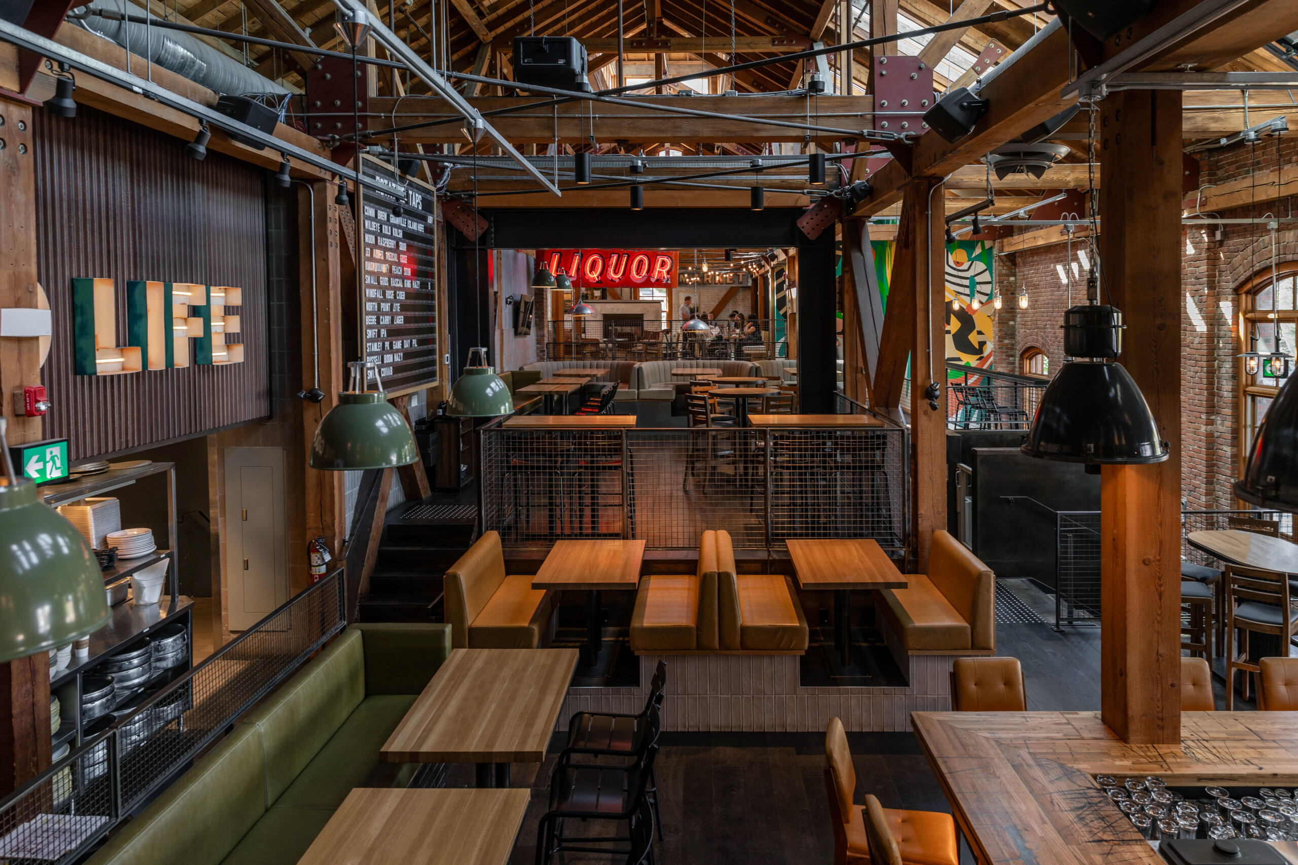 CRAFT Beer Market Spacious industrial-style restaurant interior with wooden beams, exposed brick walls, pendant lights, and empty wooden tables and booths. Neon signs read "LIFE" and "LIQUOR," setting the scene for craft beer lovers and vibrant social vibes.