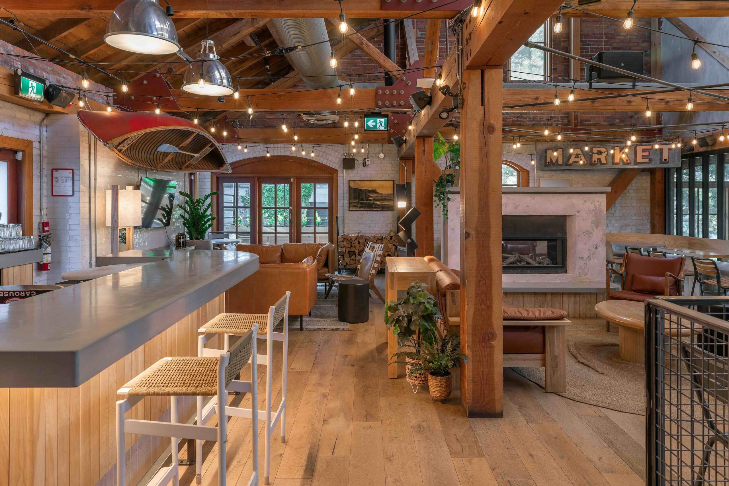 CRAFT Beer Market Spacious modern bar and lounge area with wooden beams, string lights, barstools, leather seating, plants, and a "MARKET" sign above a fireplace—perfect for social vibes and enjoying craft cocktails.