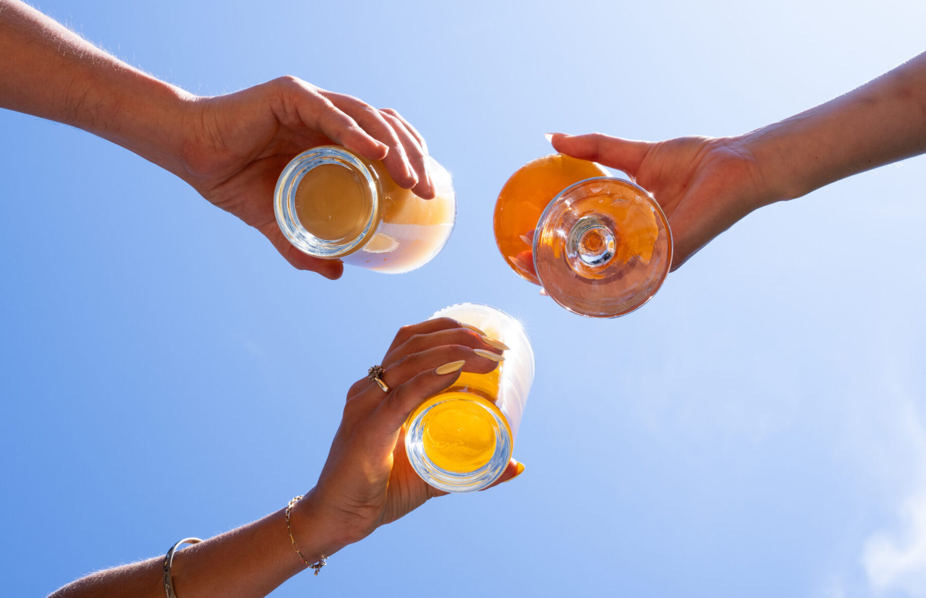 CRAFT Beer Market Three hands holding craft cocktails are raised in a toast against a clear blue sky.