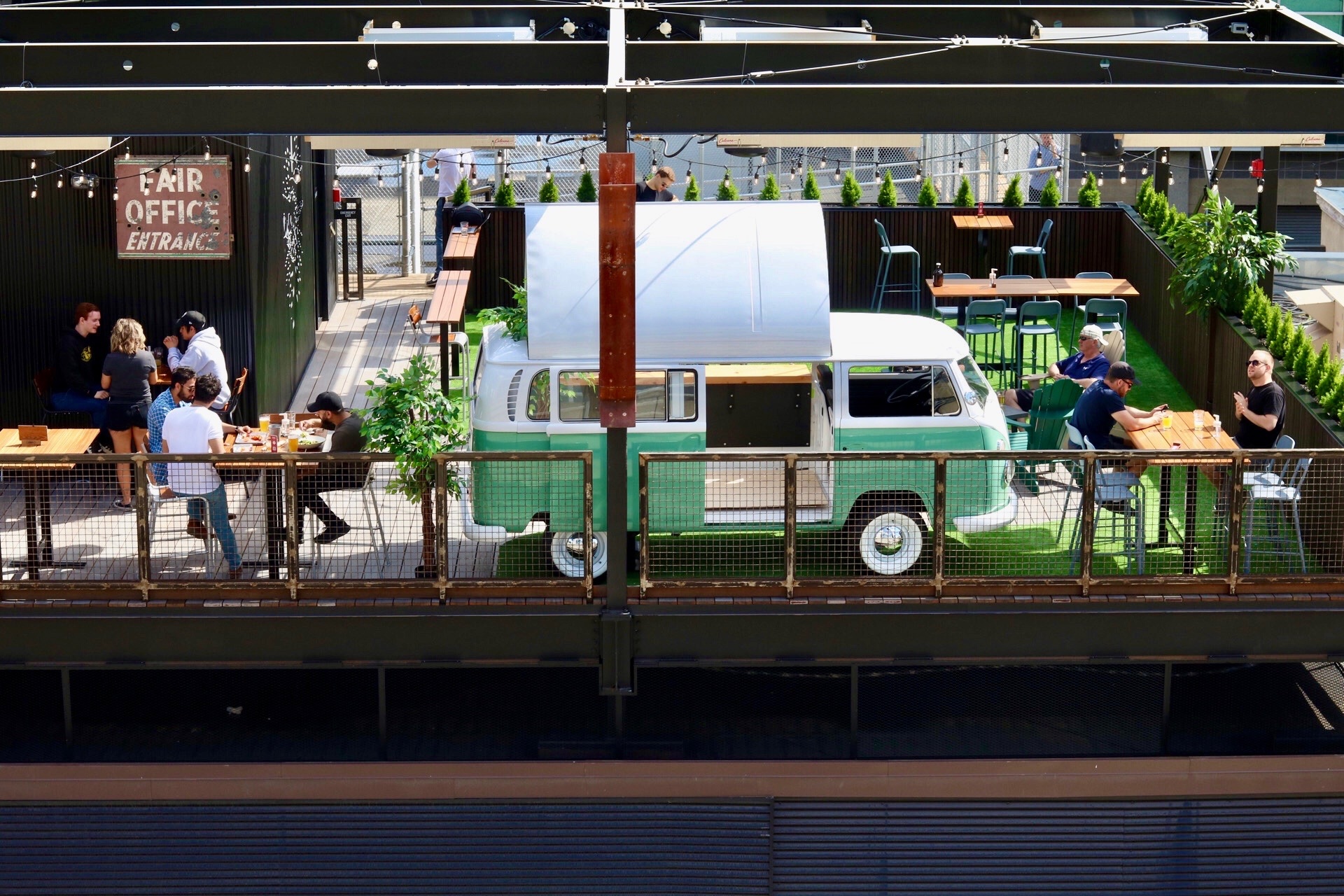 CRAFT Beer Market A rooftop cafe with outdoor seating, several people dining, and a green and white vintage van converted into a food truck at the center.