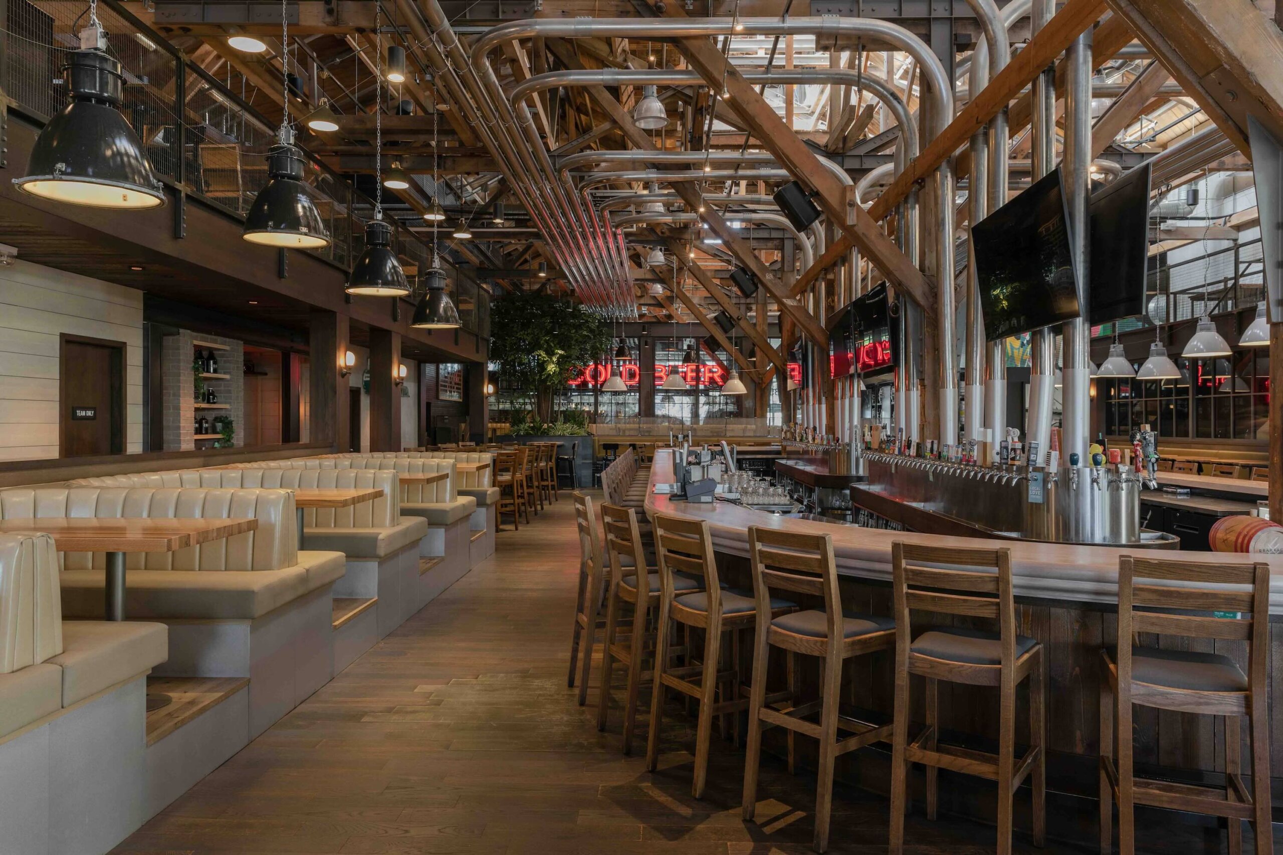 CRAFT Beer Market A modern bar and restaurant with wooden beams, high ceilings, beige booth seating, a long bar with stools, industrial lighting, and lively social vibes—perfect for enjoying craft beer with friends.