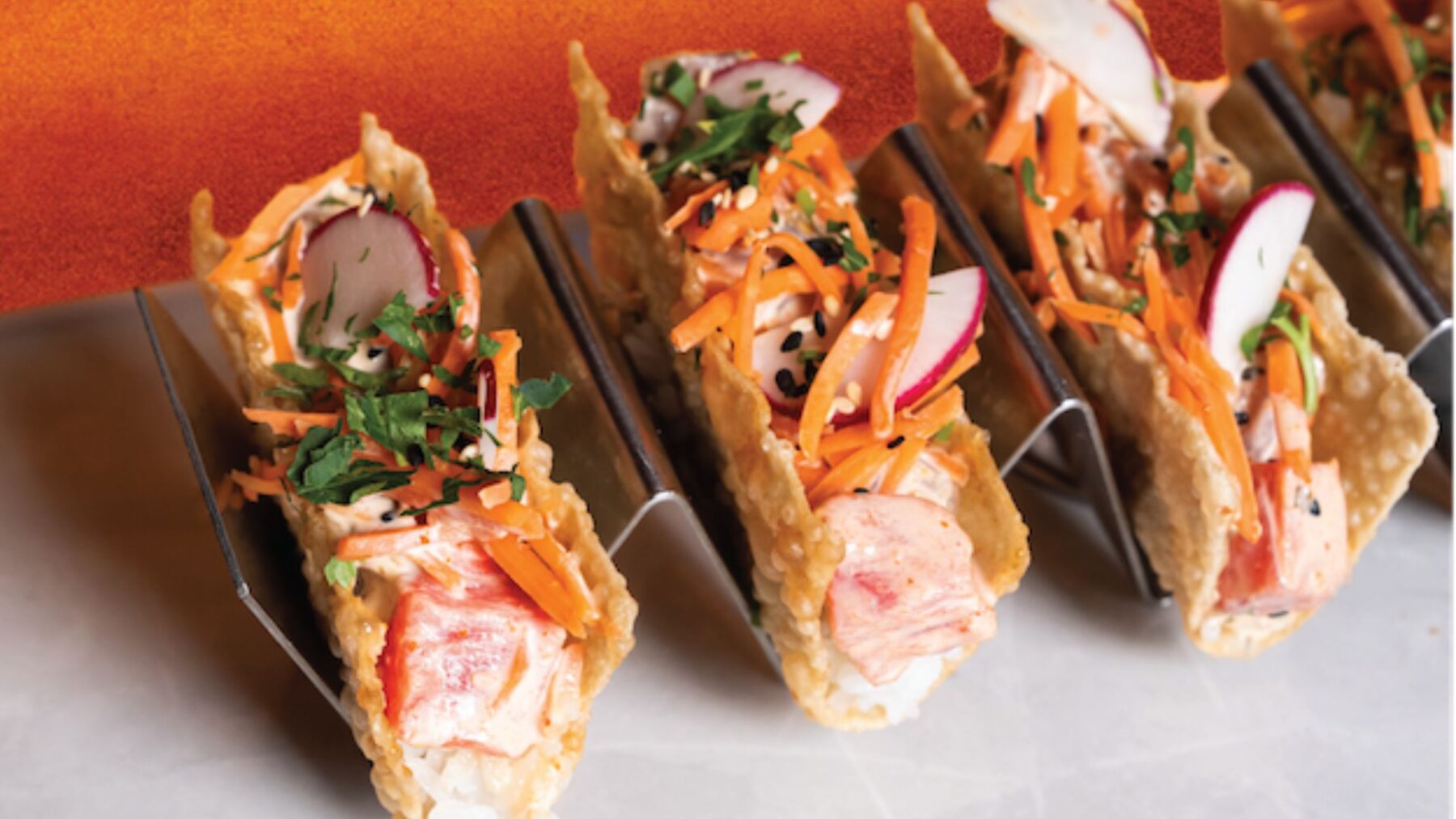 CRAFT Beer Market Three crispy tacos filled with lobster, shredded carrots, sliced radish, herbs, and sesame seeds are arranged in a metal taco holder—perfect for group bookings or paired with our craft cocktails at multiple locations.