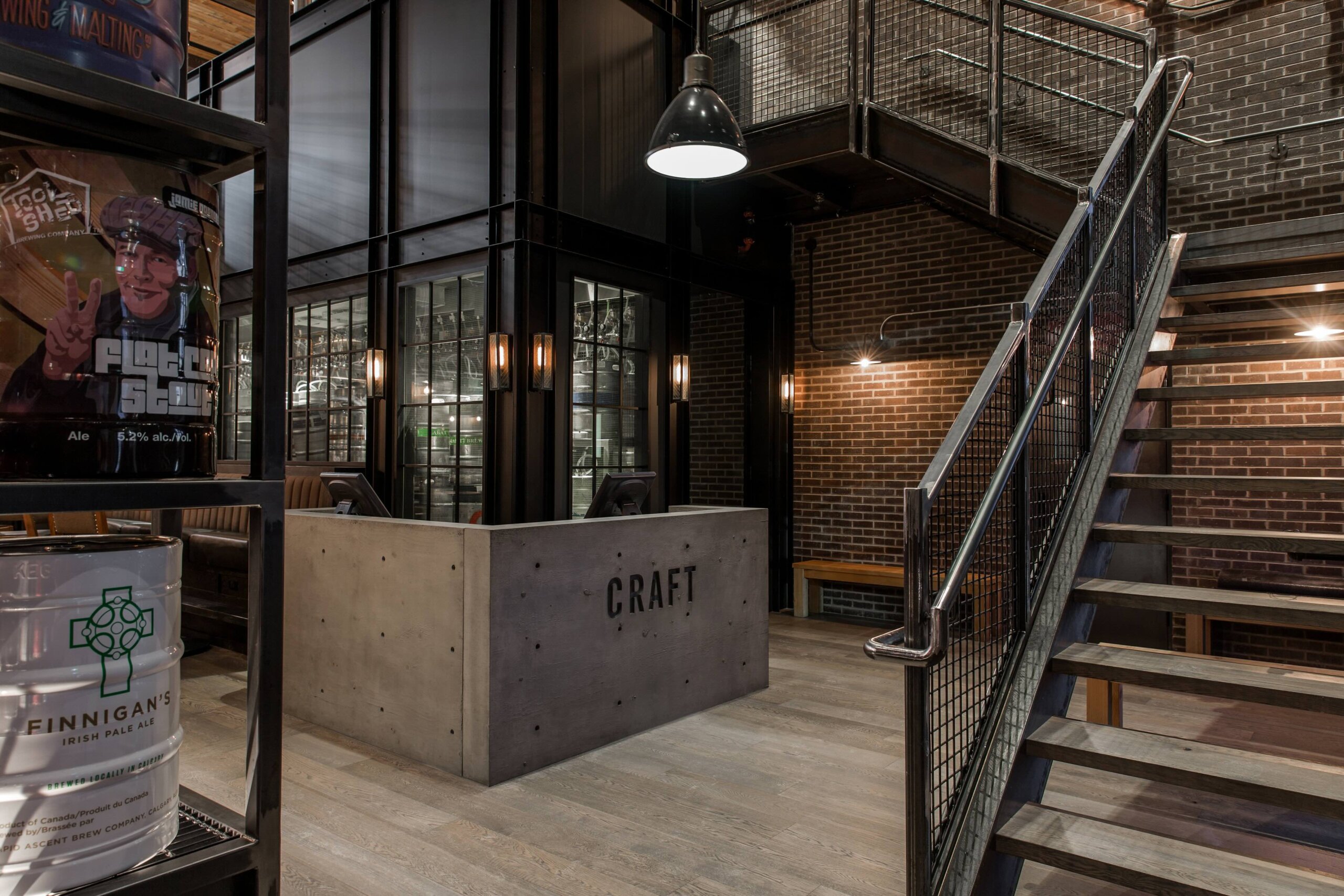 CRAFT Beer Market Industrial-style brewery or restaurant interior with metal staircase, brick walls, a concrete host stand labeled "CRAFT," and beer kegs on display.