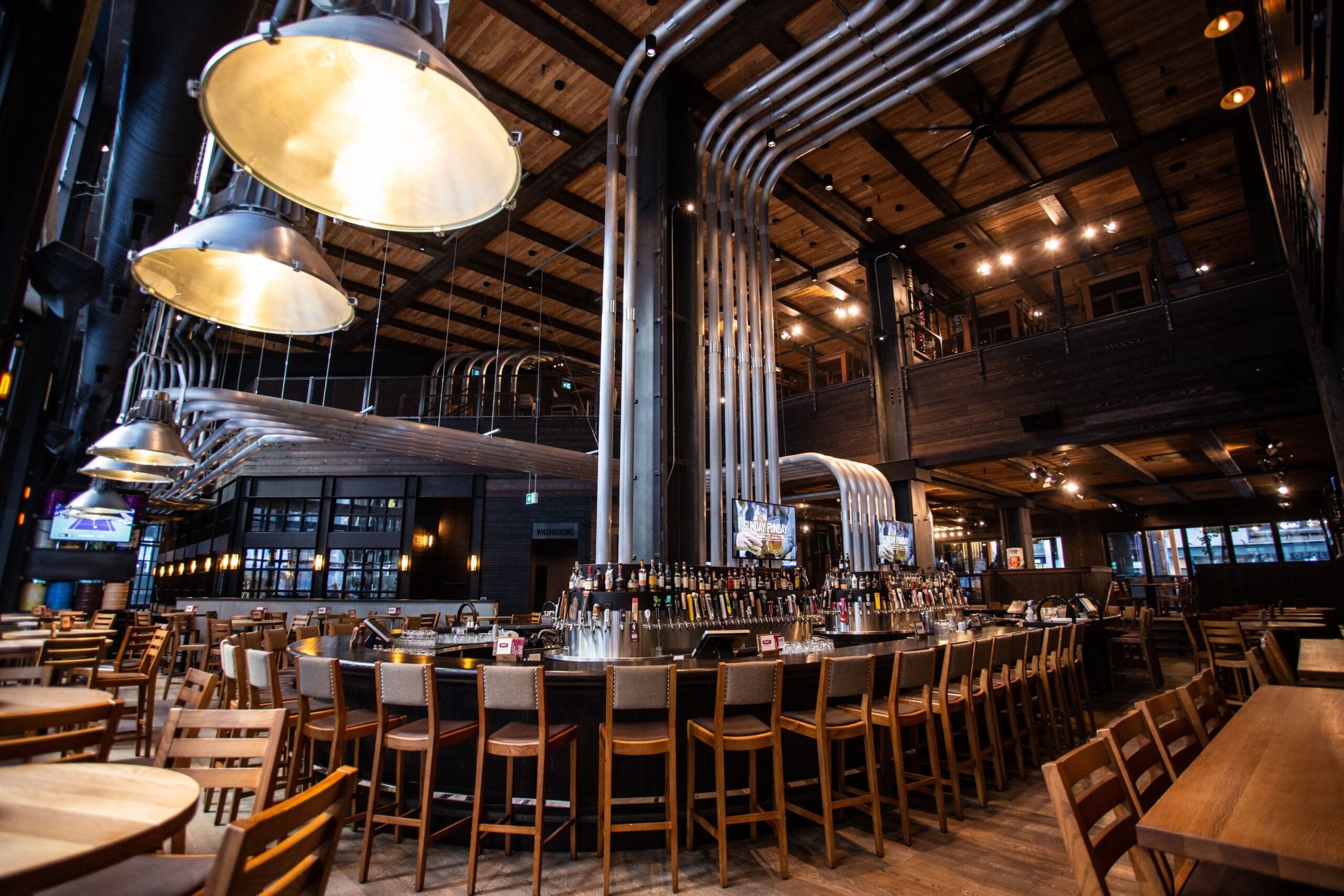 CRAFT Beer Market Spacious bar and restaurant with industrial-style metal piping, wooden tables and chairs, large hanging lights, and multiple televisions on the walls.