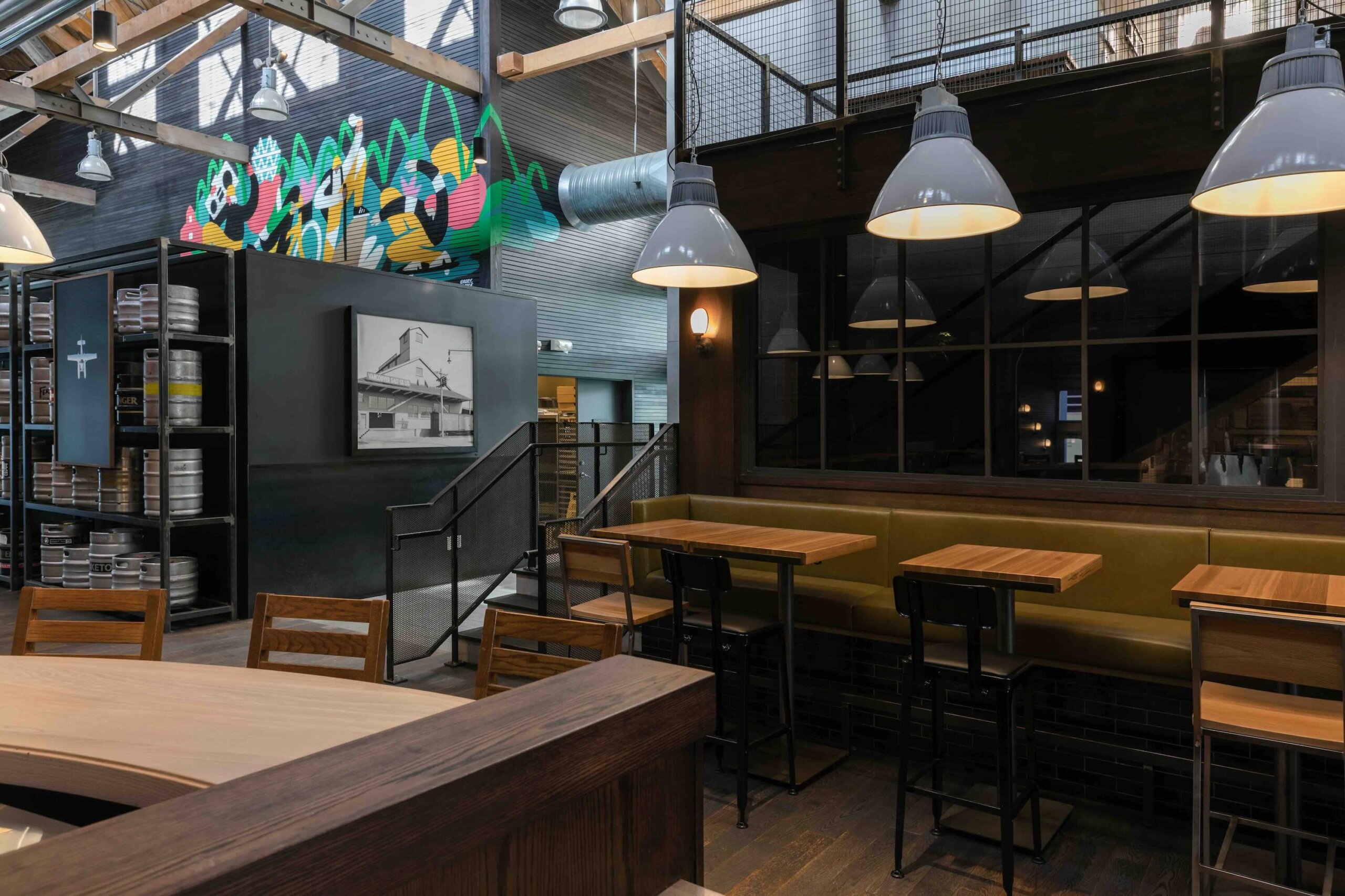 CRAFT Beer Market Modern industrial-style restaurant interior with wooden tables and chairs, hanging pendant lights, wall art, and a colorful mural in the background—perfect for casual dining or enjoying craft cocktails.