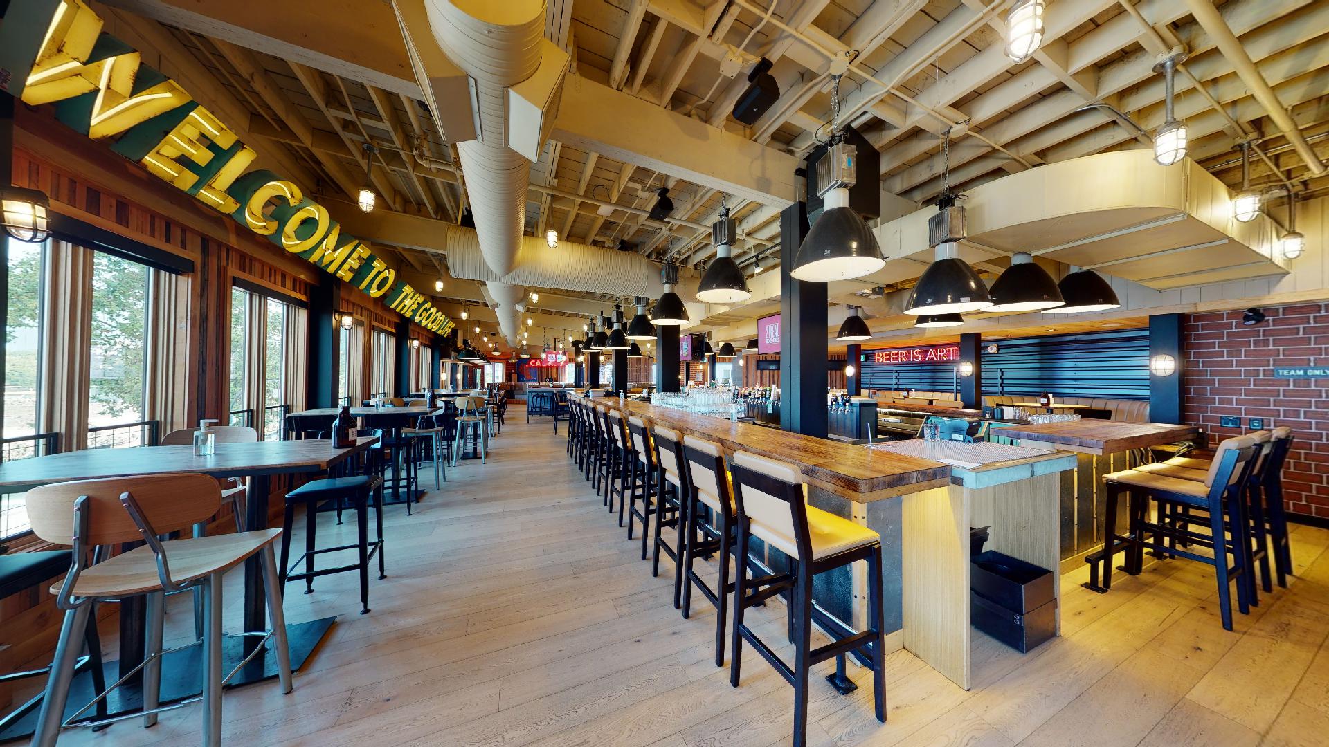 CRAFT Beer Market Spacious restaurant interior with wooden floors, high ceilings, bar seating, tables, large windows, and a "Welcome to Market" sign.