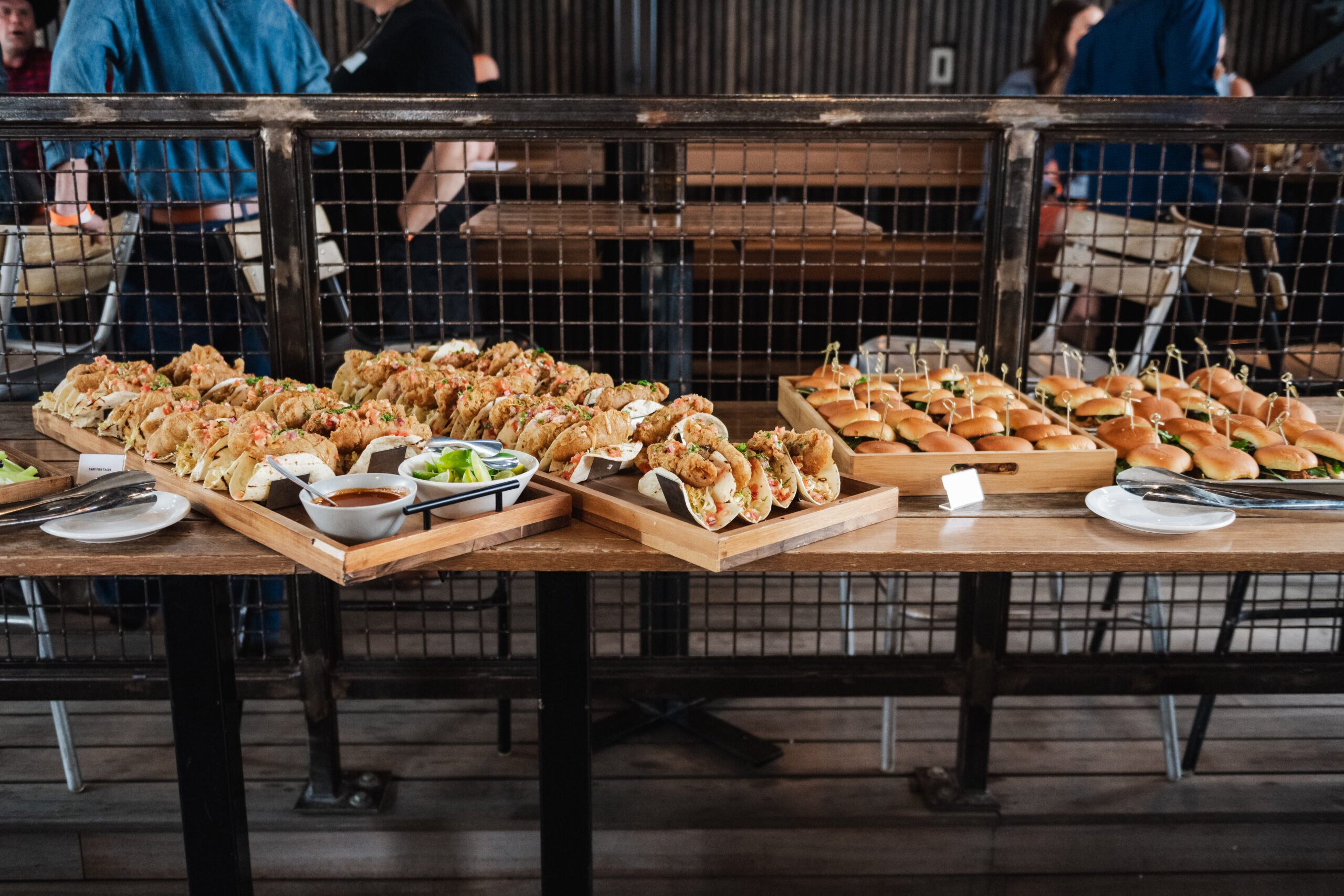 CRAFT Beer Market A buffet table with trays of tacos, sliders, dipping sauces, lime wedges, and empty plates in a casual indoor setting—perfect for group bookings and featuring delicious fare made from locally sourced ingredients.