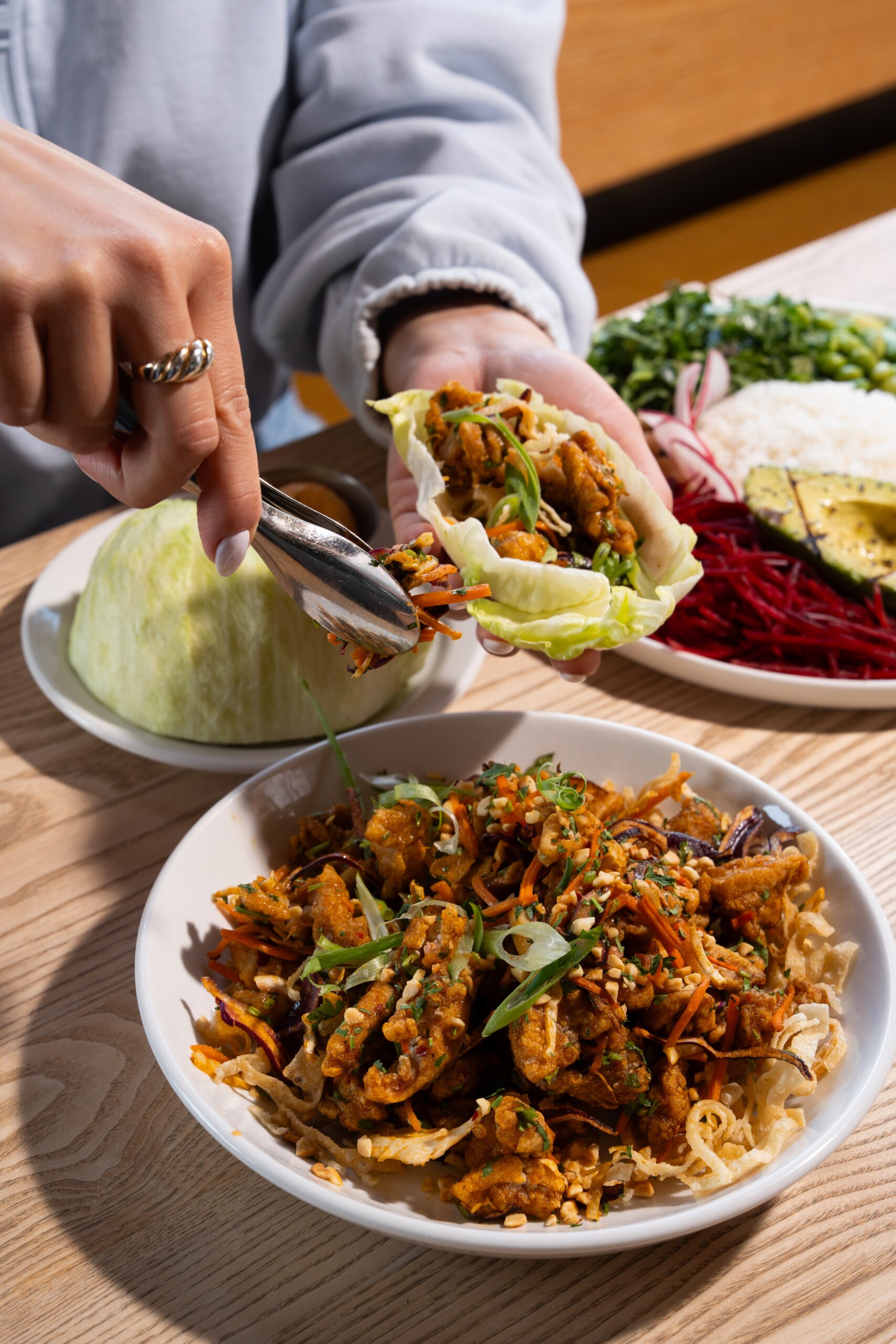 CRAFT Beer Market A person fills a lettuce leaf with a mixture of crispy fried vegetables from a bowl, creating a sustainable snack, with assorted fresh ingredients on a plate in the background.